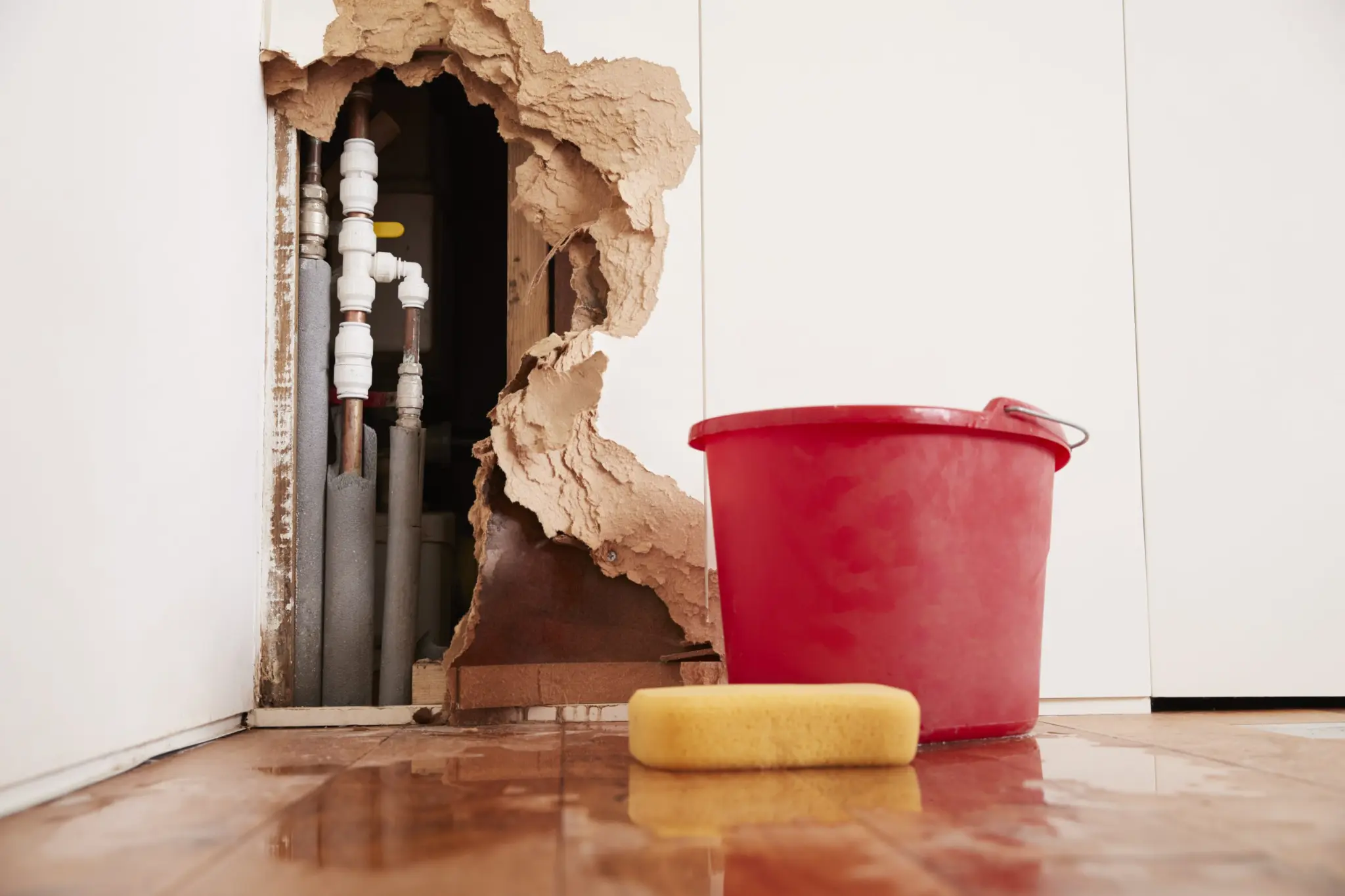 Visible leak damage — broken wall exposing pipes and water-damaged flooring in a residential property